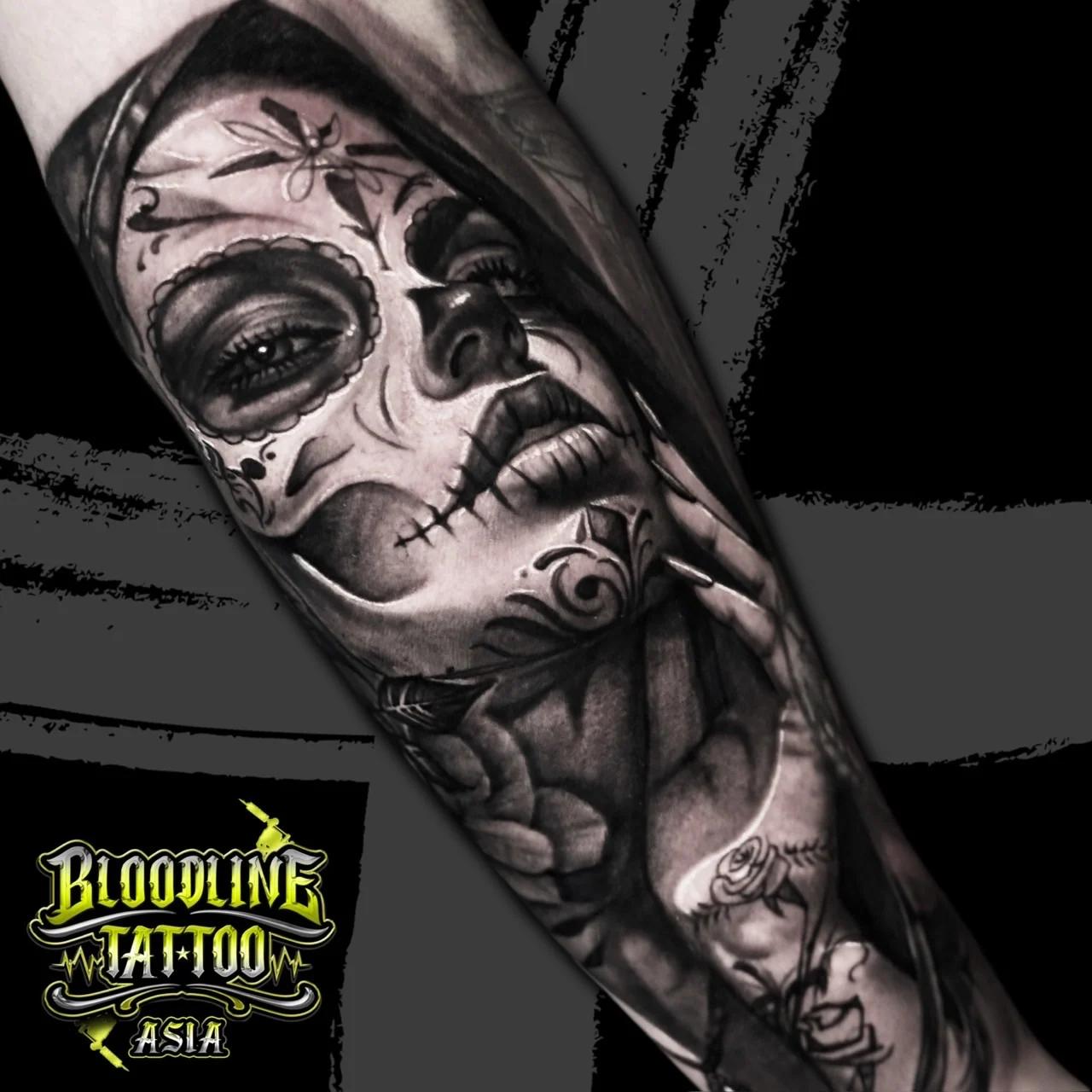 Detailed black and grey Chicano forearm tattoo of a hooded payasa Catrina portrait with ornate face paint and a rose on the hand at Bloodline Tattoo Bangkok.