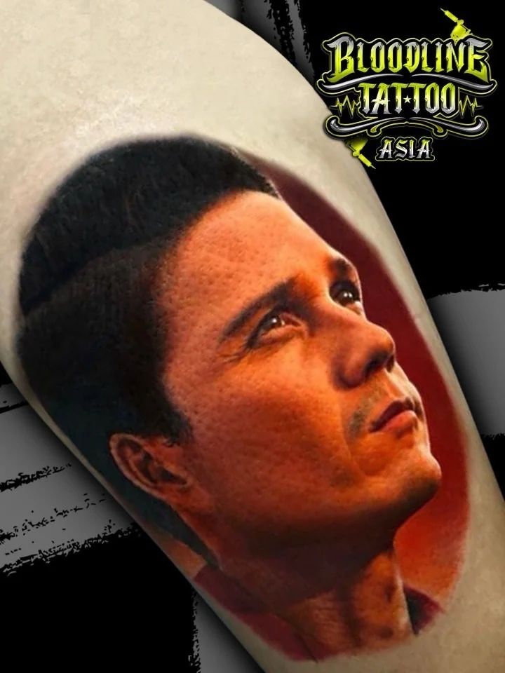 Colour portrait realism tattoo of a man in three-quarter profile with warm skin tones on the forearm at Bloodline Tattoo Bangkok.