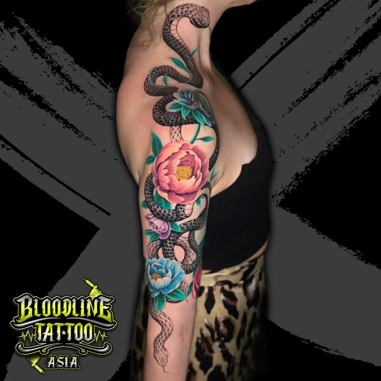 Colour arm tattoo of a black and grey snake winding through pink, purple, and blue flowers on a partial sleeve at Bloodline Tattoo Bangkok.