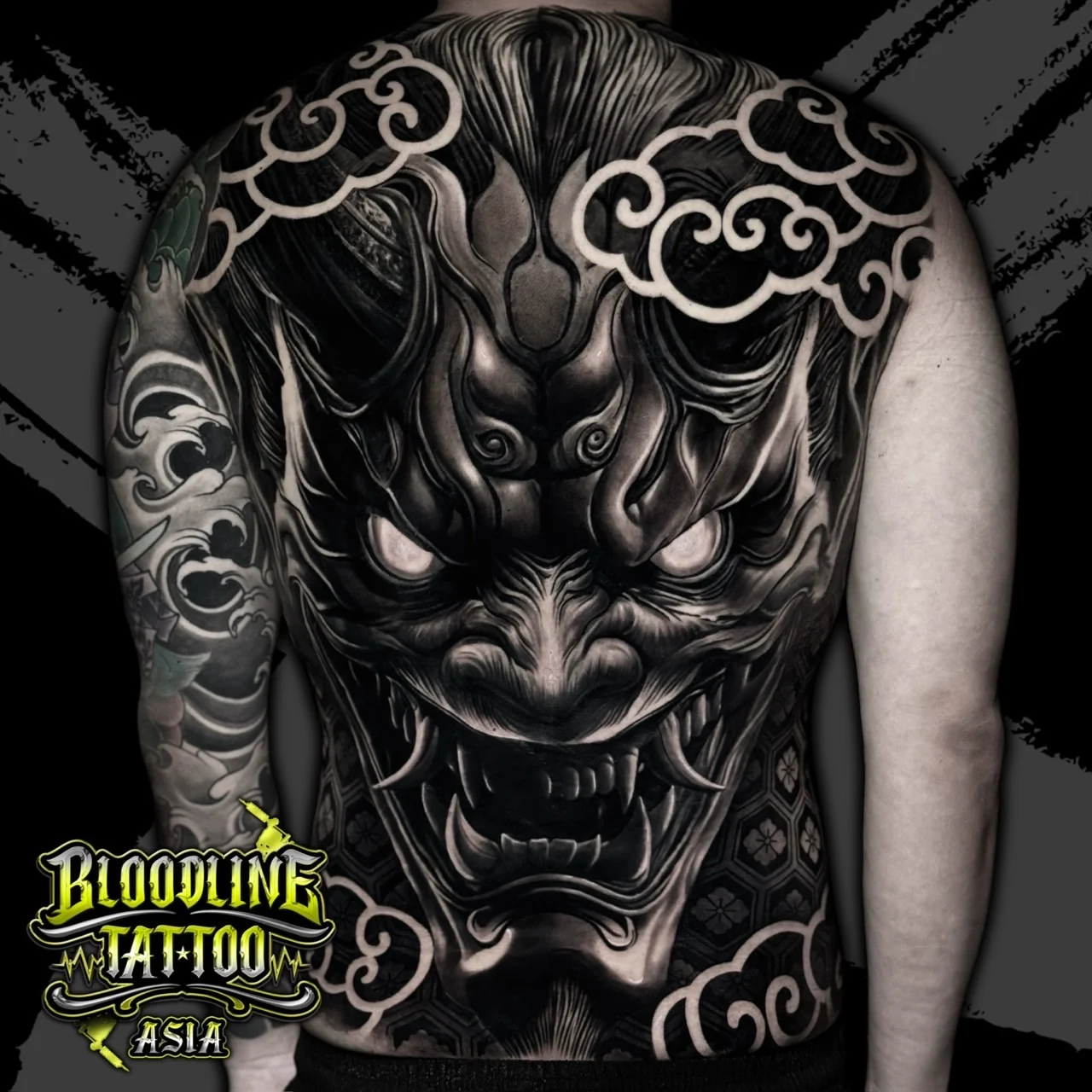 Black and grey Japanese full back Hannya mask tattoo with glowing eyes, clouds, and kikkō pattern at Bloodline Tattoo Bangkok.