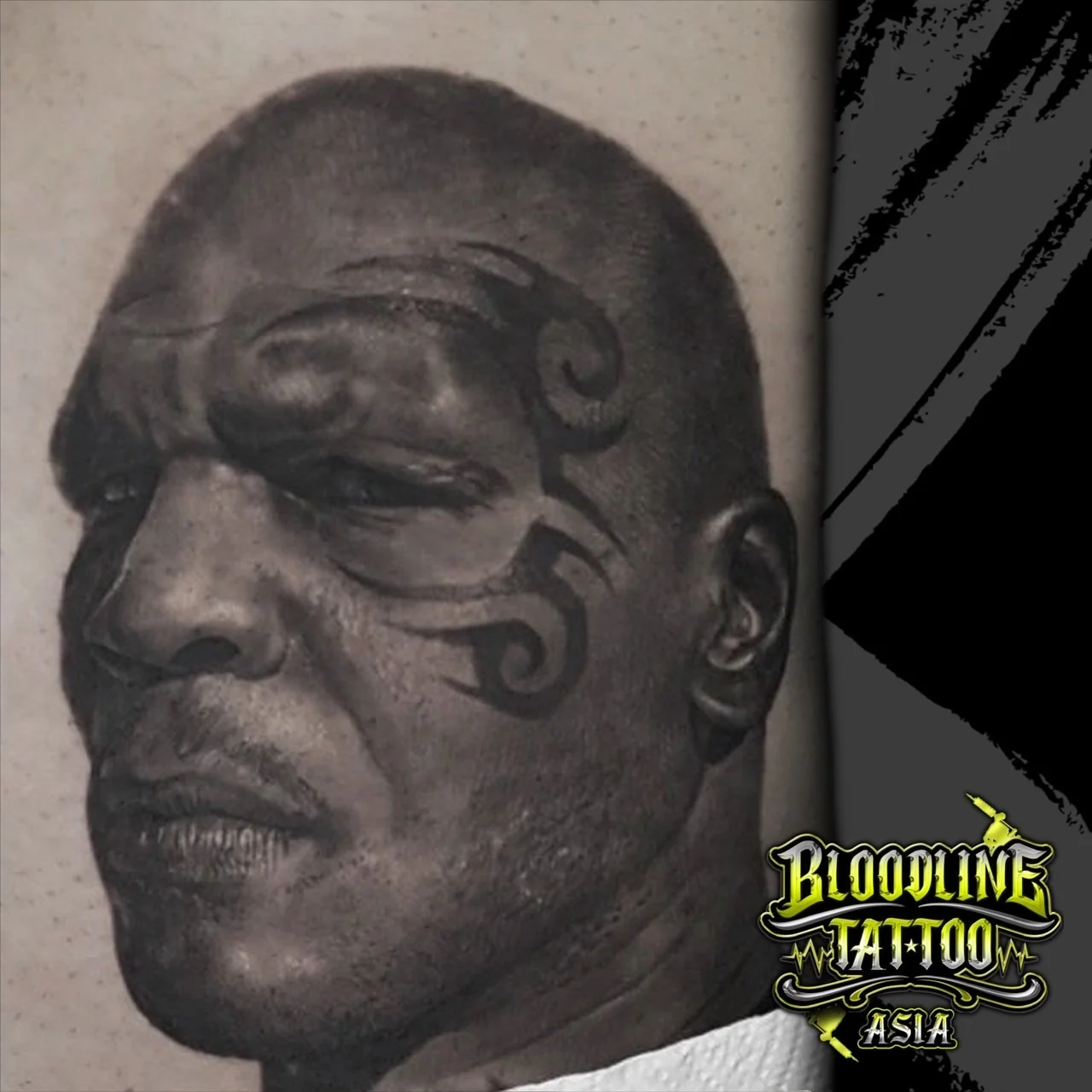 Black and grey portrait realism close-up tattoo of Mike Tyson with iconic tribal face tattoo and detailed stubble shading at Bloodline Tattoo Bangkok.