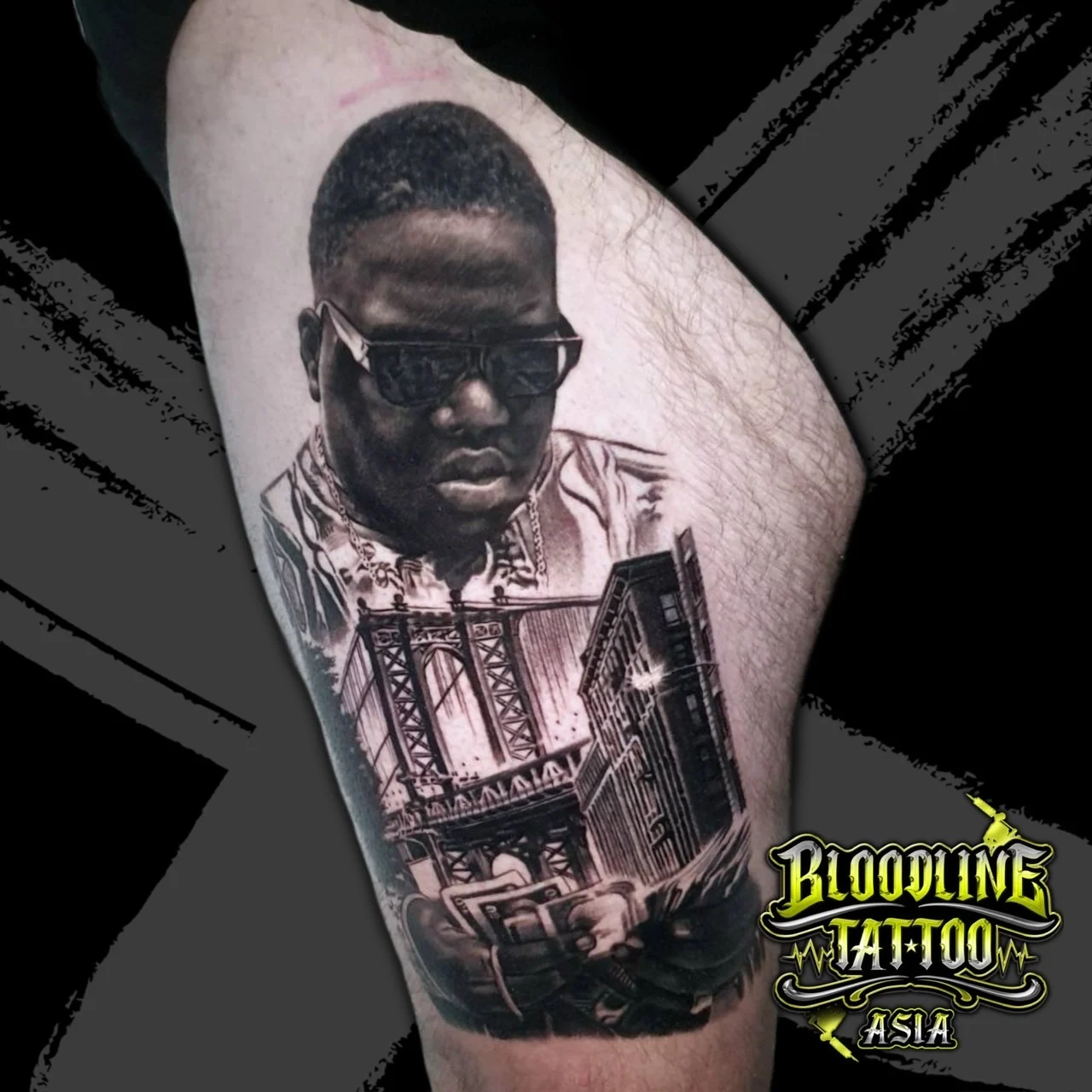 Black and grey portrait realism leg tattoo of The Notorious B.I.G. in sunglasses with Manhattan Bridge skyline and hands holding cash at Bloodline Tattoo Bangkok.