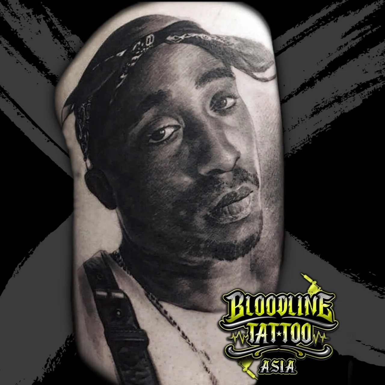 Black and grey portrait realism shoulder tattoo of Tupac Shakur wearing a front-tied bandana with chain and strap detail at Bloodline Tattoo Bangkok.