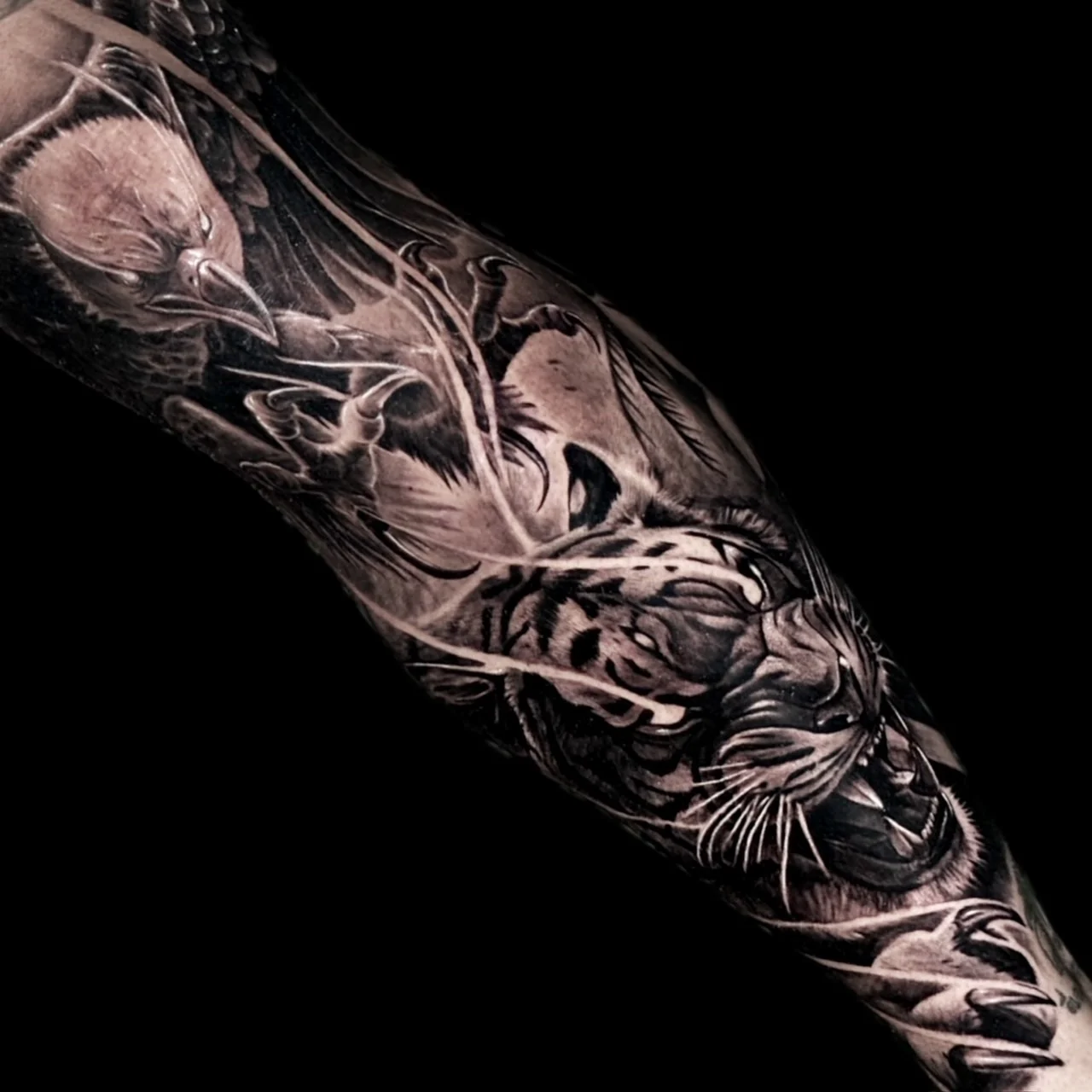 A black and grey realism sleeve with a bald eagle above a snarling tiger's head, connected by wispy lightning-like energy streaks, at Bloodline Tattoo Bangkok.